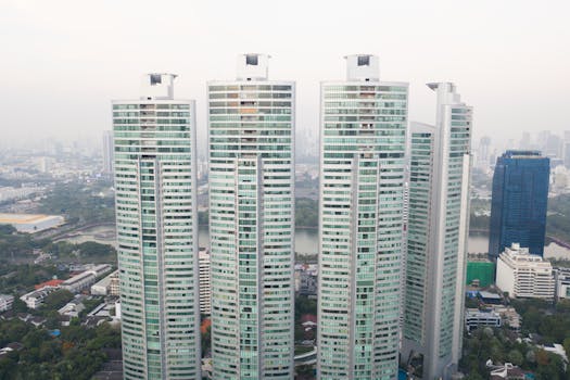 Distance view of contemporary high buildings located near green urban park in megalopolis downtown district against foggy day sky background