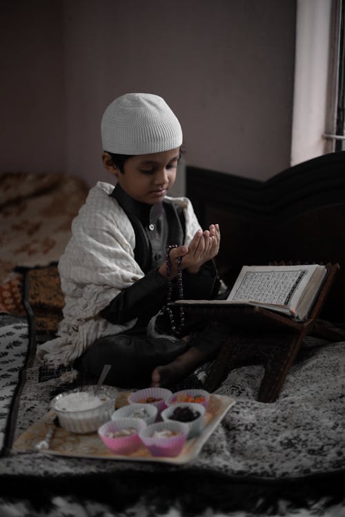 Muslim Boy Studying Quran Next to Tray of Cupcakes