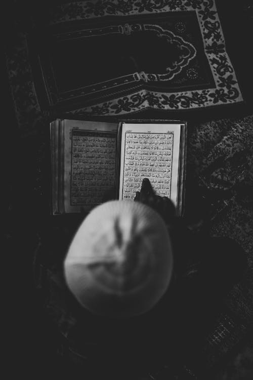 Free From above of unrecognizable person in hat sitting on rug and reading interesting thick book in retro fashioned room alone Stock Photo