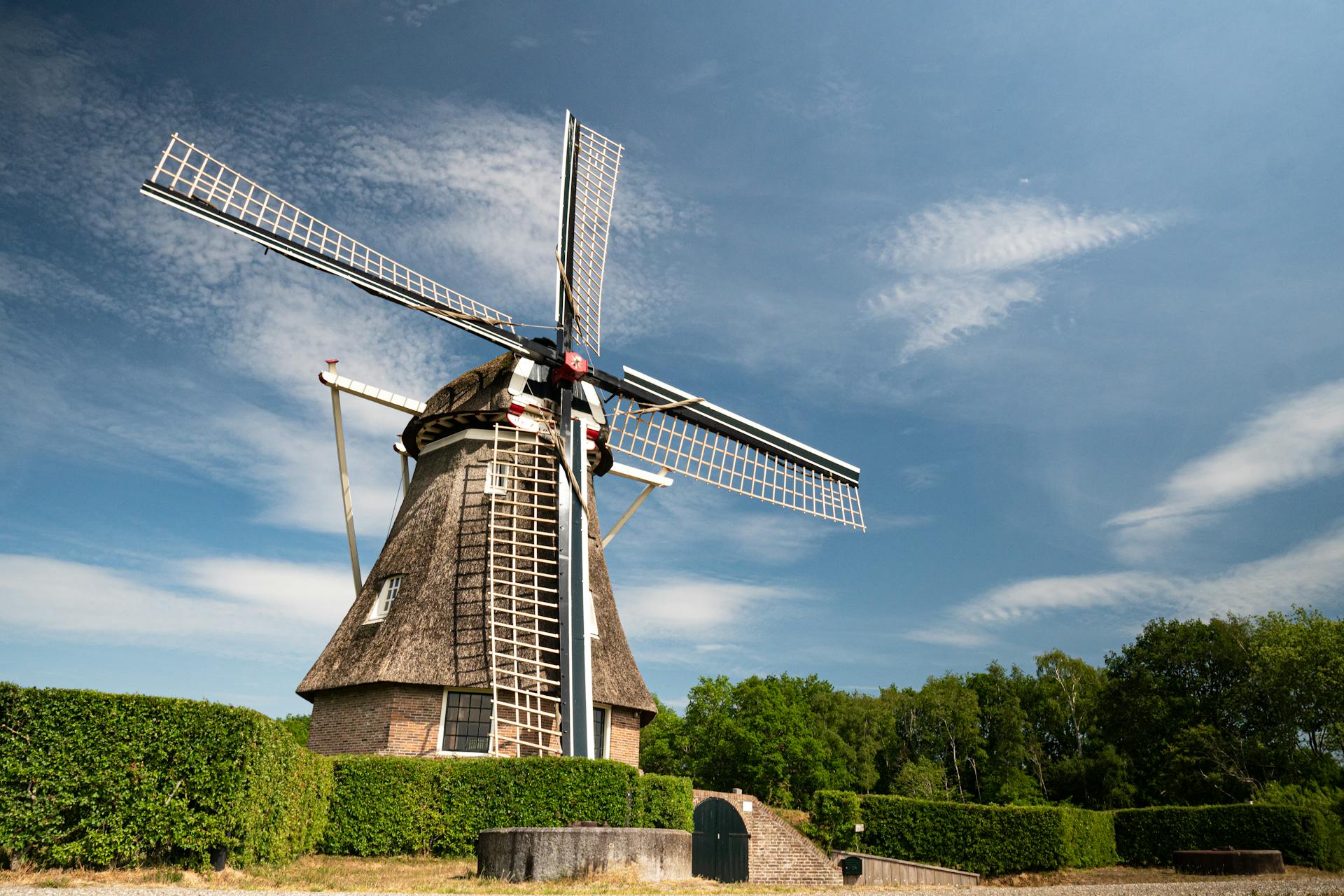 Low angle of aged of big mill in green plants against cloudy sky at sunny day