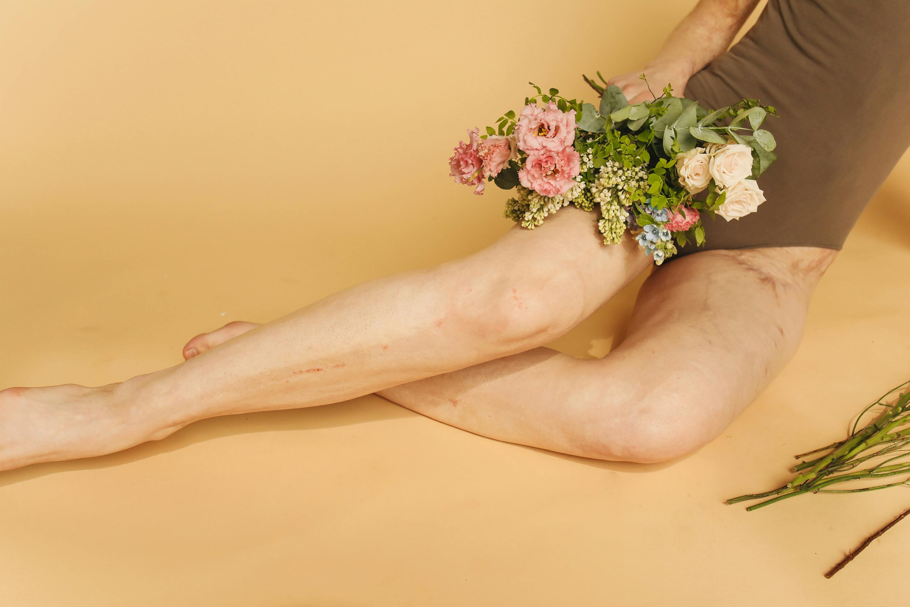 A creative arrangement of flowers and legs against a soft yellow background.