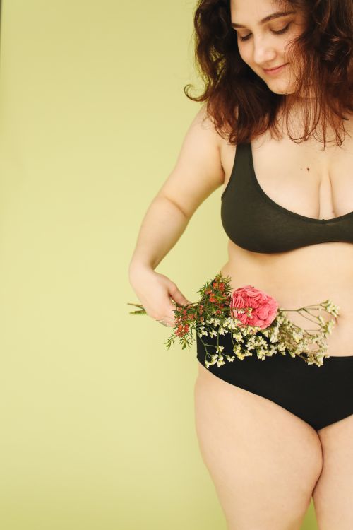 Free Confident woman embracing body positivity with flowers in studio. Stock Photo