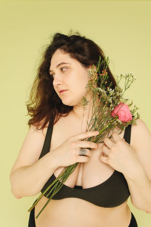 Free A plus-size woman in a studio setting holding a bouquet of wildflowers against a yellow backdrop. Stock Photo