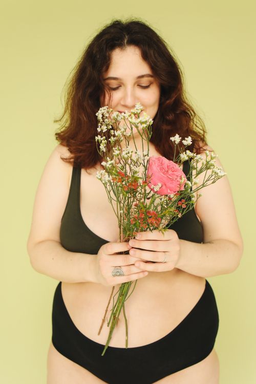 Free Portrait of a plus size woman holding flowers against a yellow background. Stock Photo