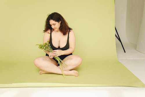 Free Woman in Black Brassiere Sitting on the Floor while Looking at the Green Plant she is Holding Stock Photo