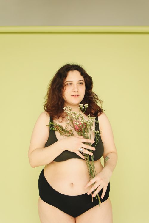 Free Portrait of a woman embracing body positivity, holding flowers in a studio. Stock Photo