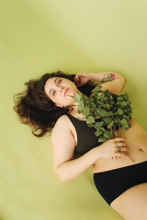Free Creative studio portrait of a woman posing with eucalyptus leaves on a green backdrop. Stock Photo