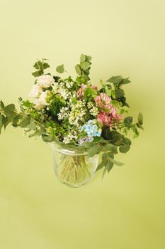 透明玻璃花瓶中，一束令人惊叹的混合花优雅地排列着，衬托着绿色背景