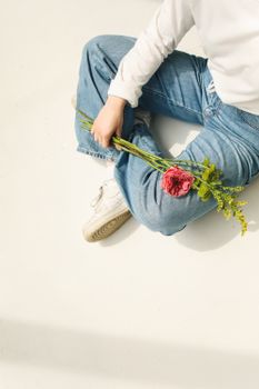 一个穿着牛仔裤的人随意地坐在室内，手里拿着花