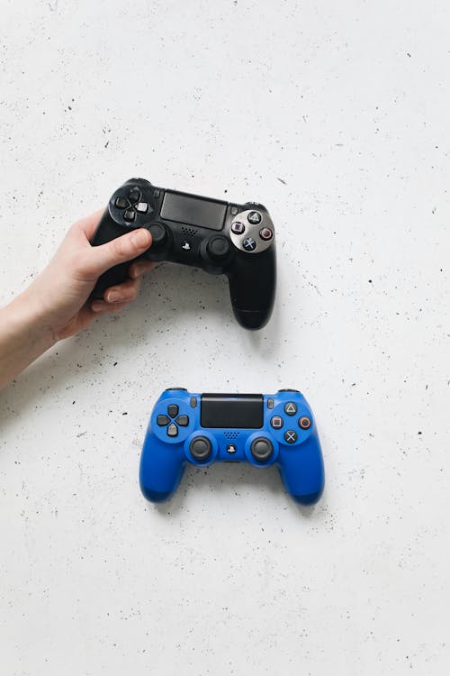 A Hand Holding Black Controller Near Blue Controller on a White Surface