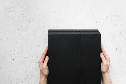 Hands holding a modern black gaming console on a textured white surface.