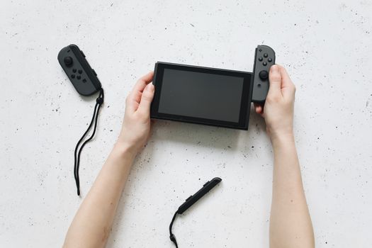 Close-up of hands assembling a Nintendo Switch console with detached controllers on a white surface.