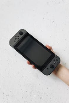 A hand holds a Nintendo Switch against a white speckled surface, showcasing the device.