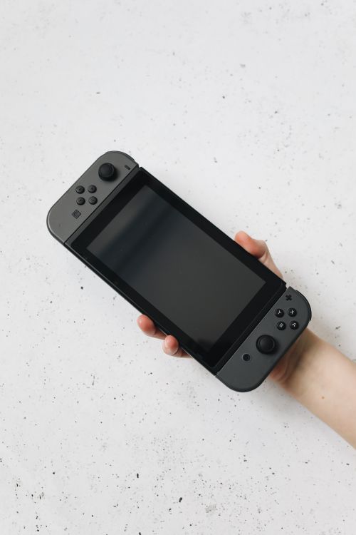 Free A hand holds a Nintendo Switch against a white speckled surface, showcasing the device. Stock Photo