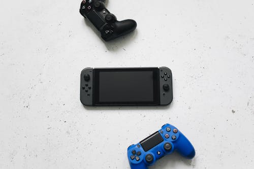 Nintendo Switch Between Playstation Controllers on a White Surface