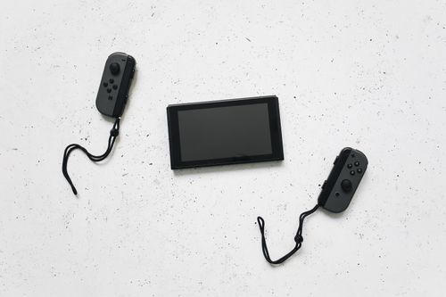 Free Flat lay of a Nintendo Switch and controllers on a white speckled surface, showcasing modern gaming tech. Stock Photo