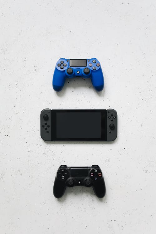 Nintendo Switch Between Playstation Controllers on a White Surface
