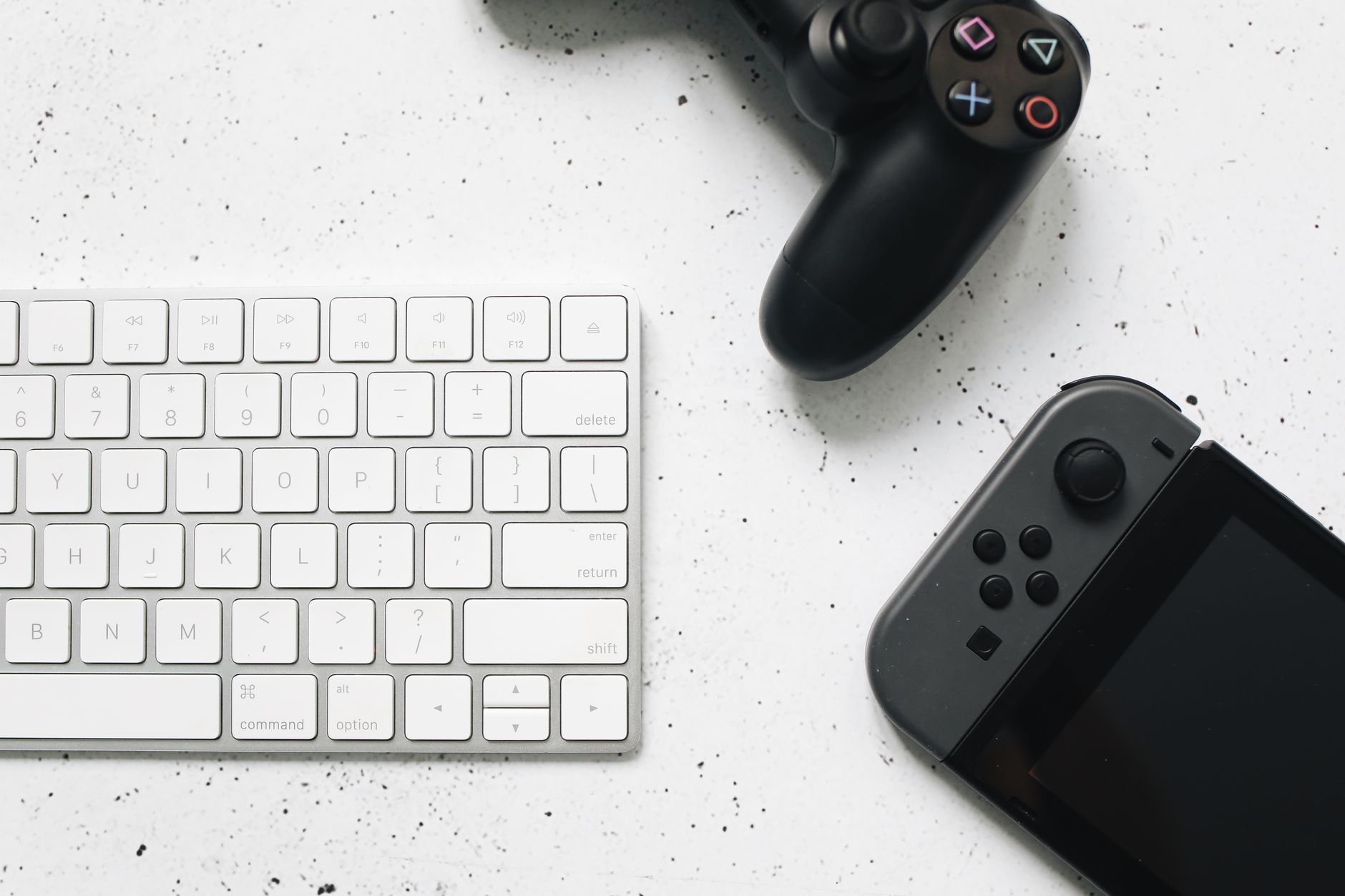 Close-up of a wireless keyboard and gaming controllers on a marble surface.