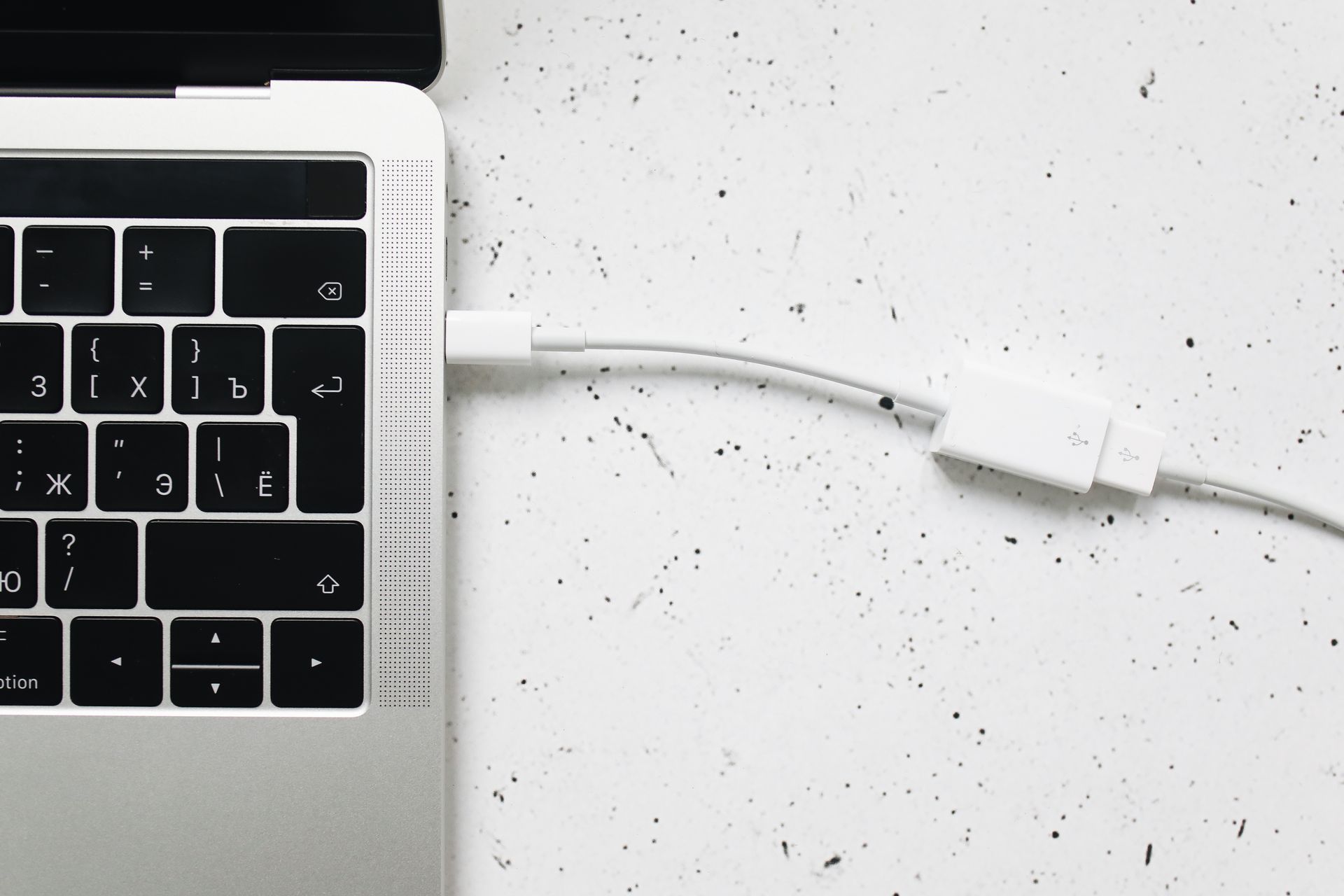Close-up of a USB cable connected to a laptop keyboard on a white textured surface.