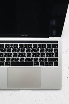 A MacBook Pro with Cyrillic keyboard on a speckled white surface, top view.