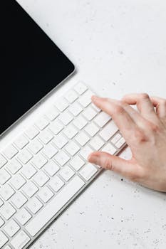 Close-up of a human hand typing on a sleek white keyboard indoors.