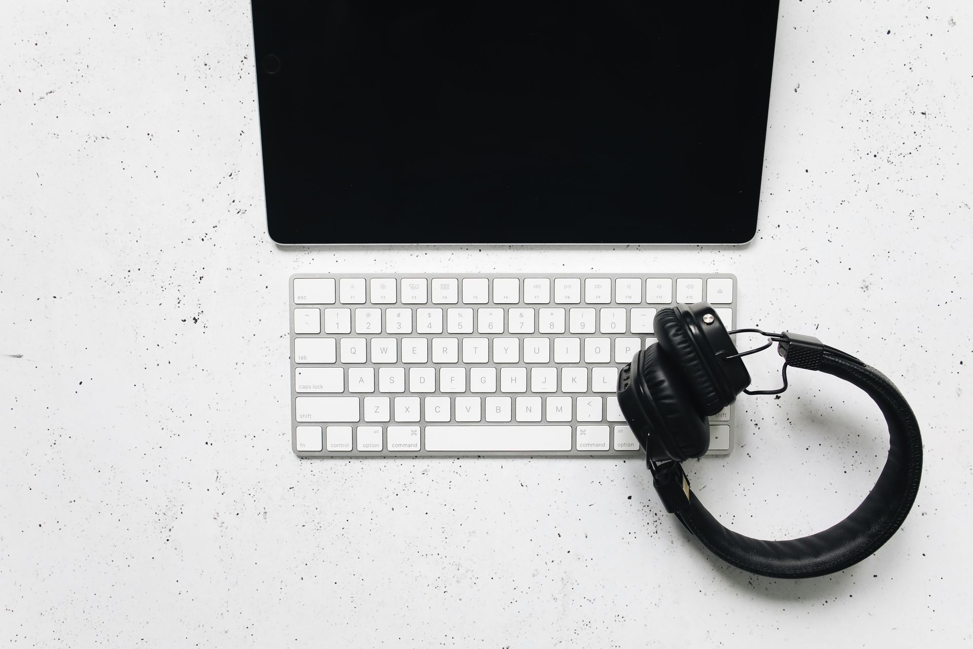 Minimalist setup featuring a tablet, keyboard, and headphones on a white desk.