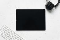 白色背景上，平放着一台数字平板电脑、一副耳机和一个键盘