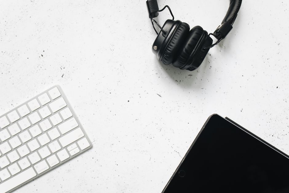 Minimalist top view of a workspace with a digital tablet, keyboard, and headphones on a white background.