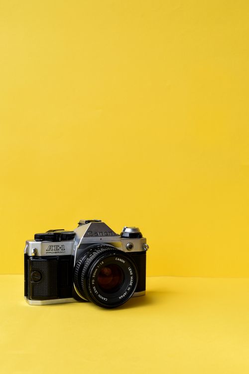 Free Classic vintage film camera against a vivid yellow backdrop, evoking nostalgia and retro elegance. Stock Photo