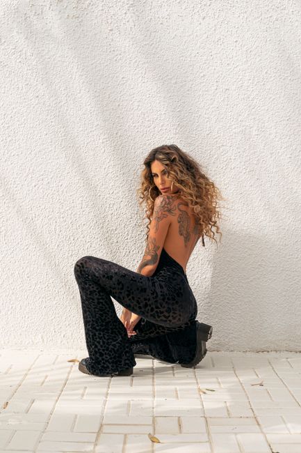 Fashionable woman with tattoos posing against a textured wall in sunlight.
