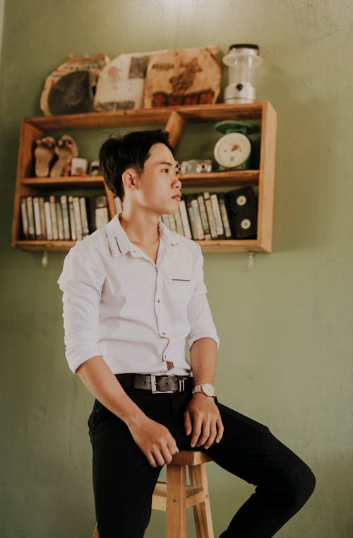 Stylish dreamy Asian man on stool at home