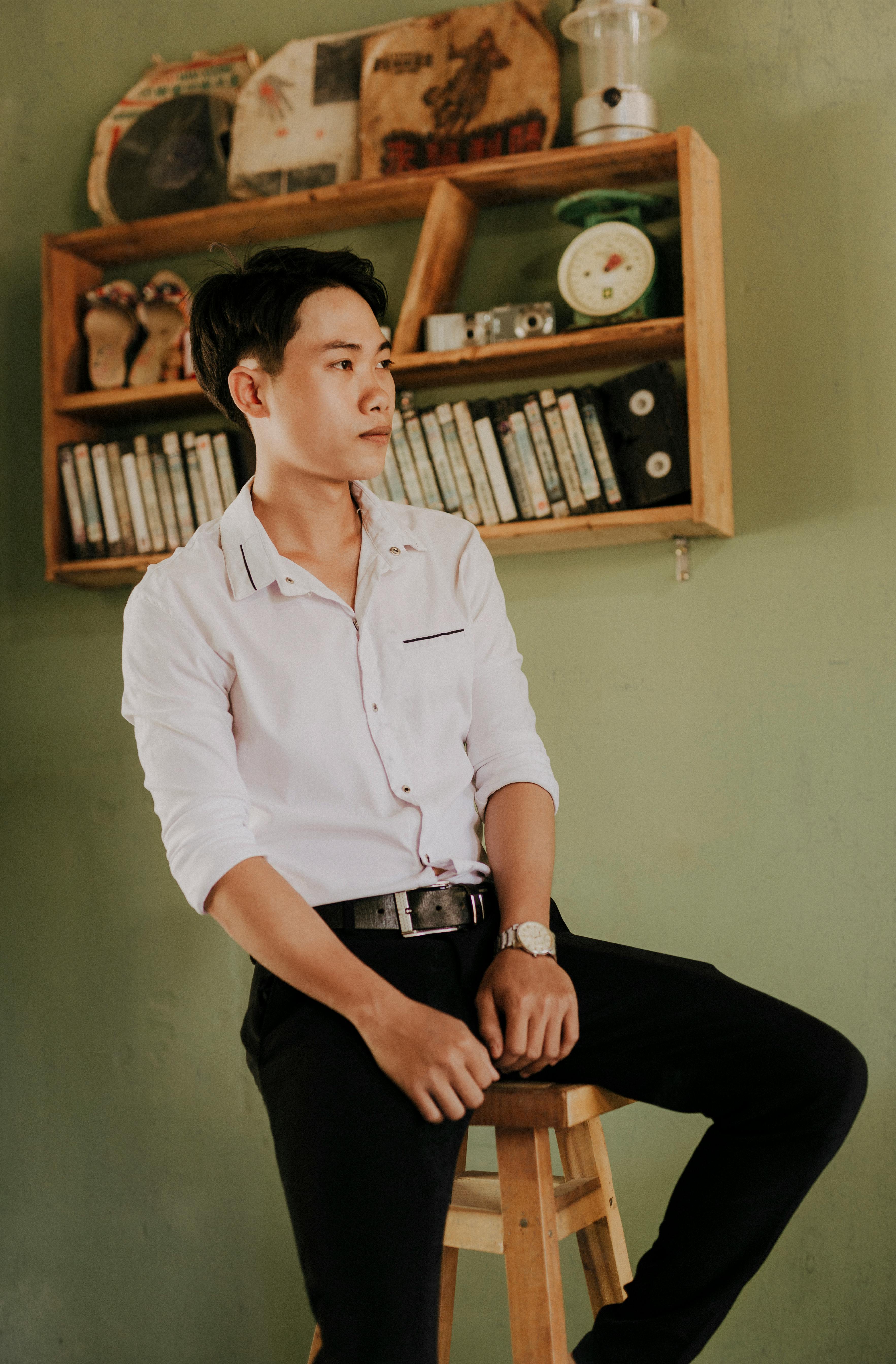 wistful asian man in trendy clothes resting on stool