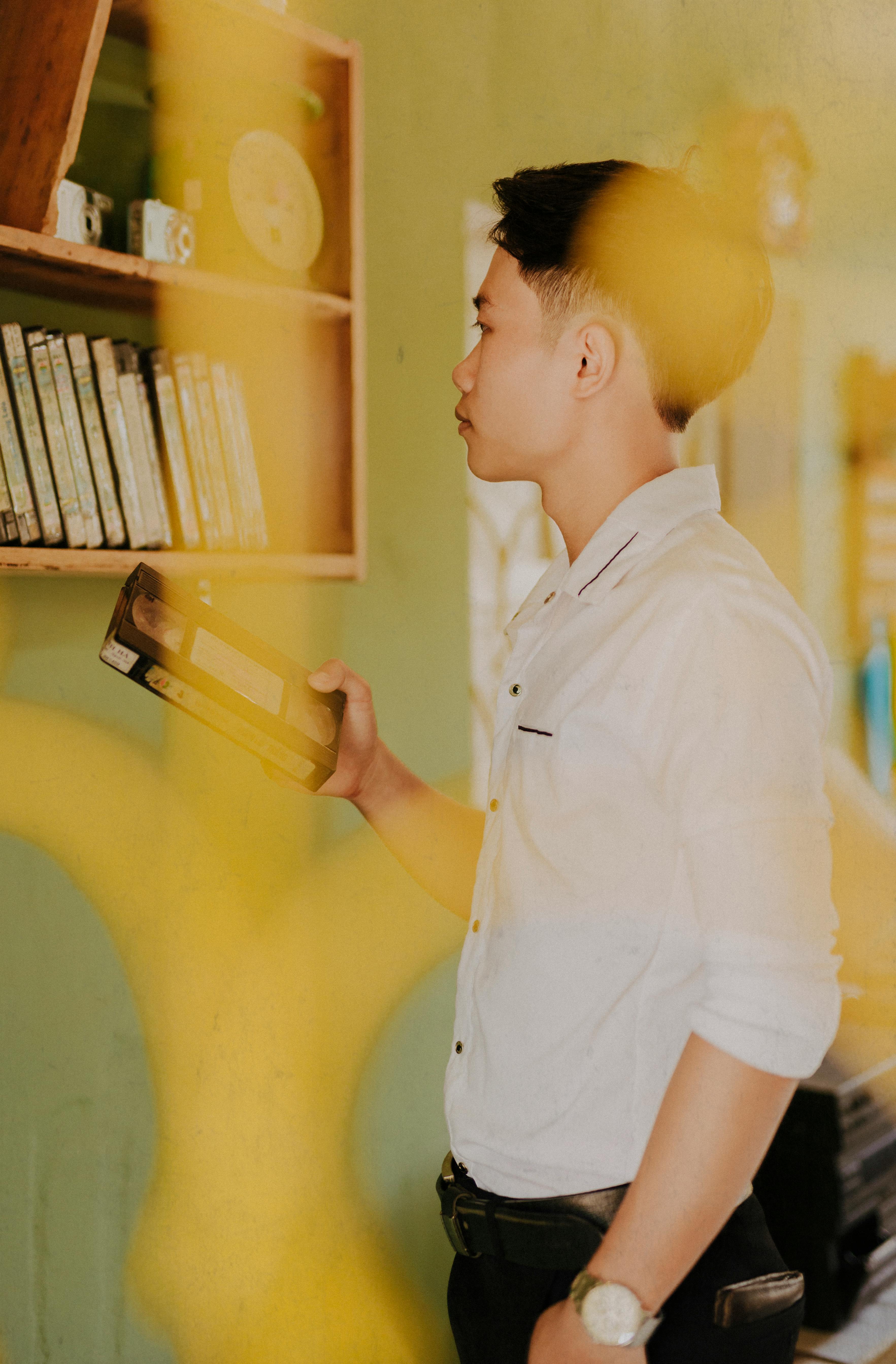 thoughtful trendy ethnic man choosing video tape from shelf