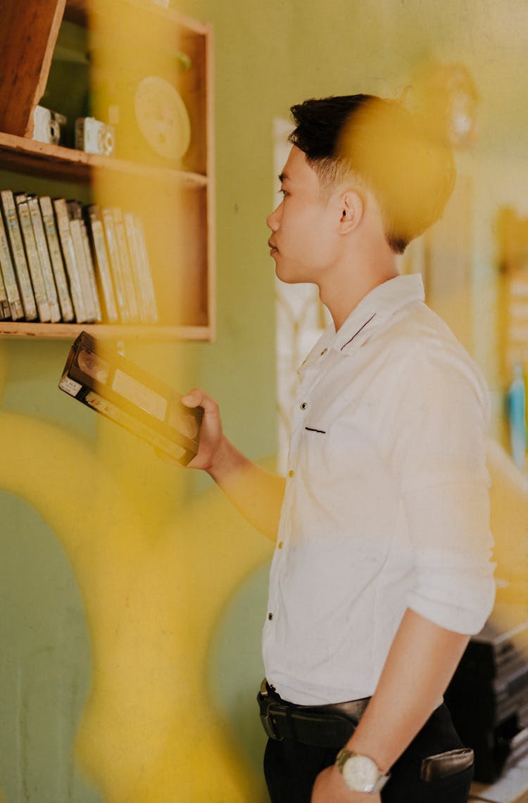 Thoughtful Trendy Ethnic Man Choosing Video Tape From Shelf