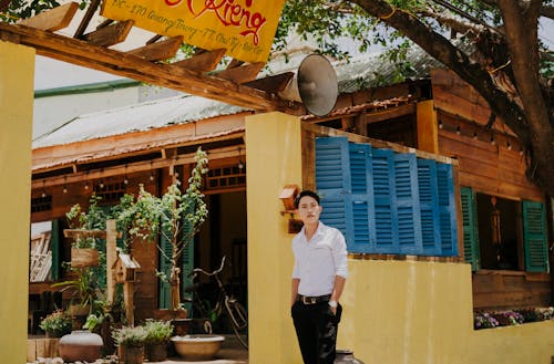 Pondering stylish ethnic man near wall of wooden house