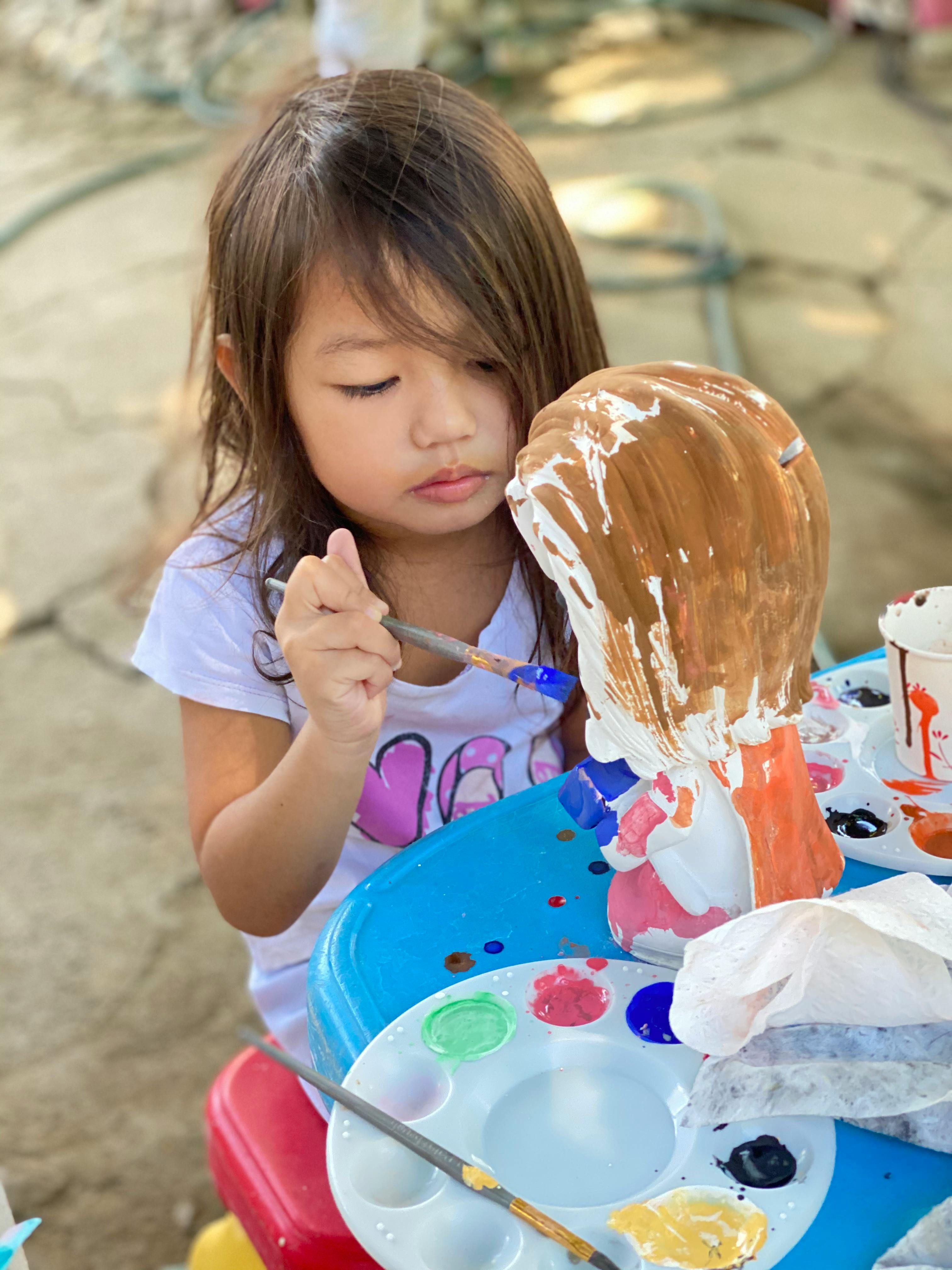 little asian girl painting doll on street