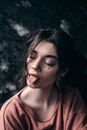 From above of young trendy female with makeup and tongue out standing with closed eyes outdoors