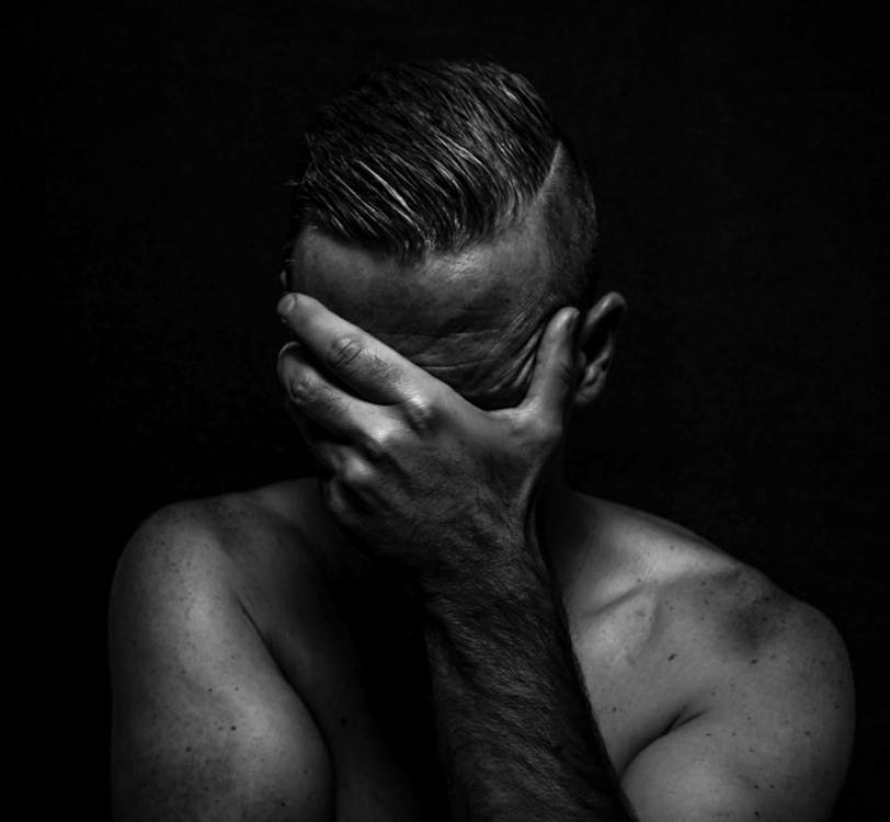 Black and white of unrecognizable fit masculine frustrated male with stylish haircut covering face with hand