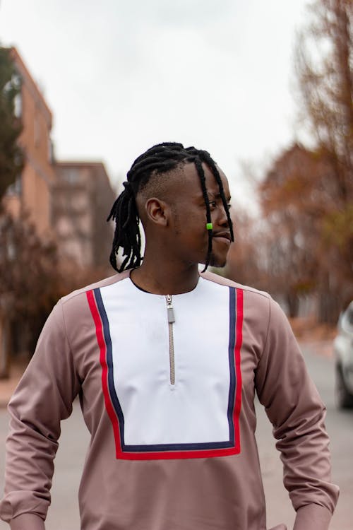 Stylish African American male with dreadlocks in casual wear looking away on city street