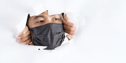 Crop attentive man in face mask behind torn paper wall