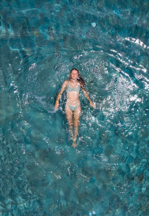 From above of young woman in bikini floating on azure calm sea water while enjoying vacation on resort