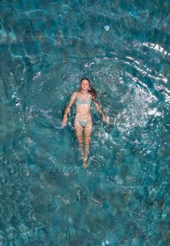 From above of young woman in bikini floating on azure calm sea water while enjoying vacation on resort