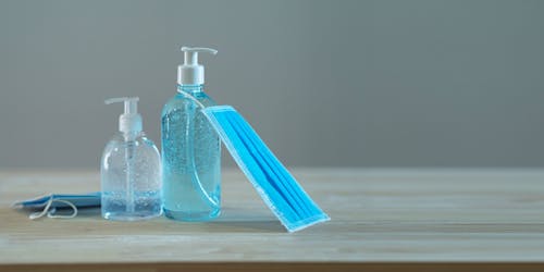 Free From above of plastic bottles with bubbled soap and sanitizer near bright face masks on wooden desk during quarantine period Stock Photo