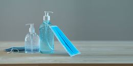 From above of plastic bottles with bubbled soap and sanitizer near bright face masks on wooden desk during quarantine period