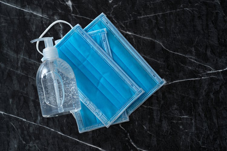 Liquid Soap Dispenser With Sterile Masks On Marble Surface