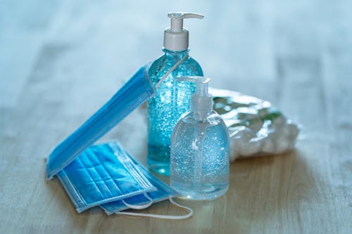 Free From above of transparent bottles with antibacterial gels near blue face masks on table during quarantine period Stock Photo