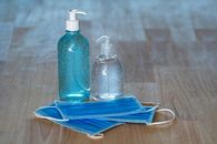 From above of transparent bottles with bubbled antiseptic liquid soap and gel near medical masks on table