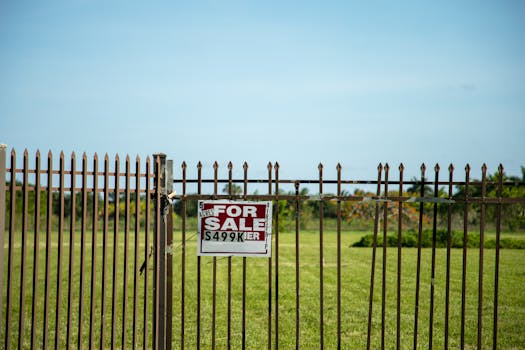A large plot of land bordered by an iron fence, complete with a 'For Sale' sign in Miami, FL. Ideal for development.