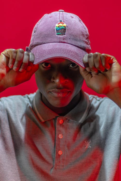 Concentrated African American male in casual wear touching cap with ornament while looking at camera