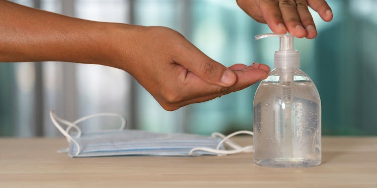 Crop Person Using Gel From Dispenser At Home